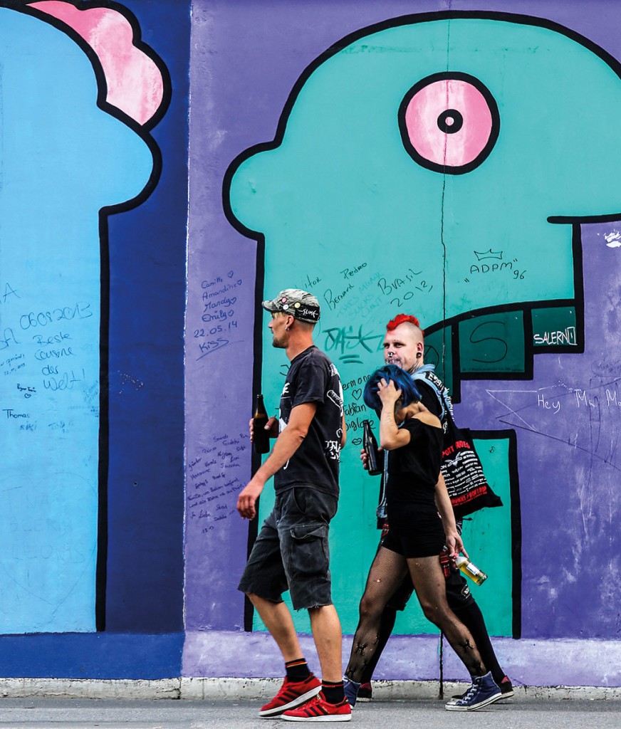 Punks walk past Heads, by artist thierry noir, at the east Side Gallery.