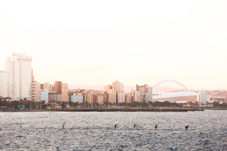 Stand up paddlers heading out to the sea, the profile of Durban city in the background. 